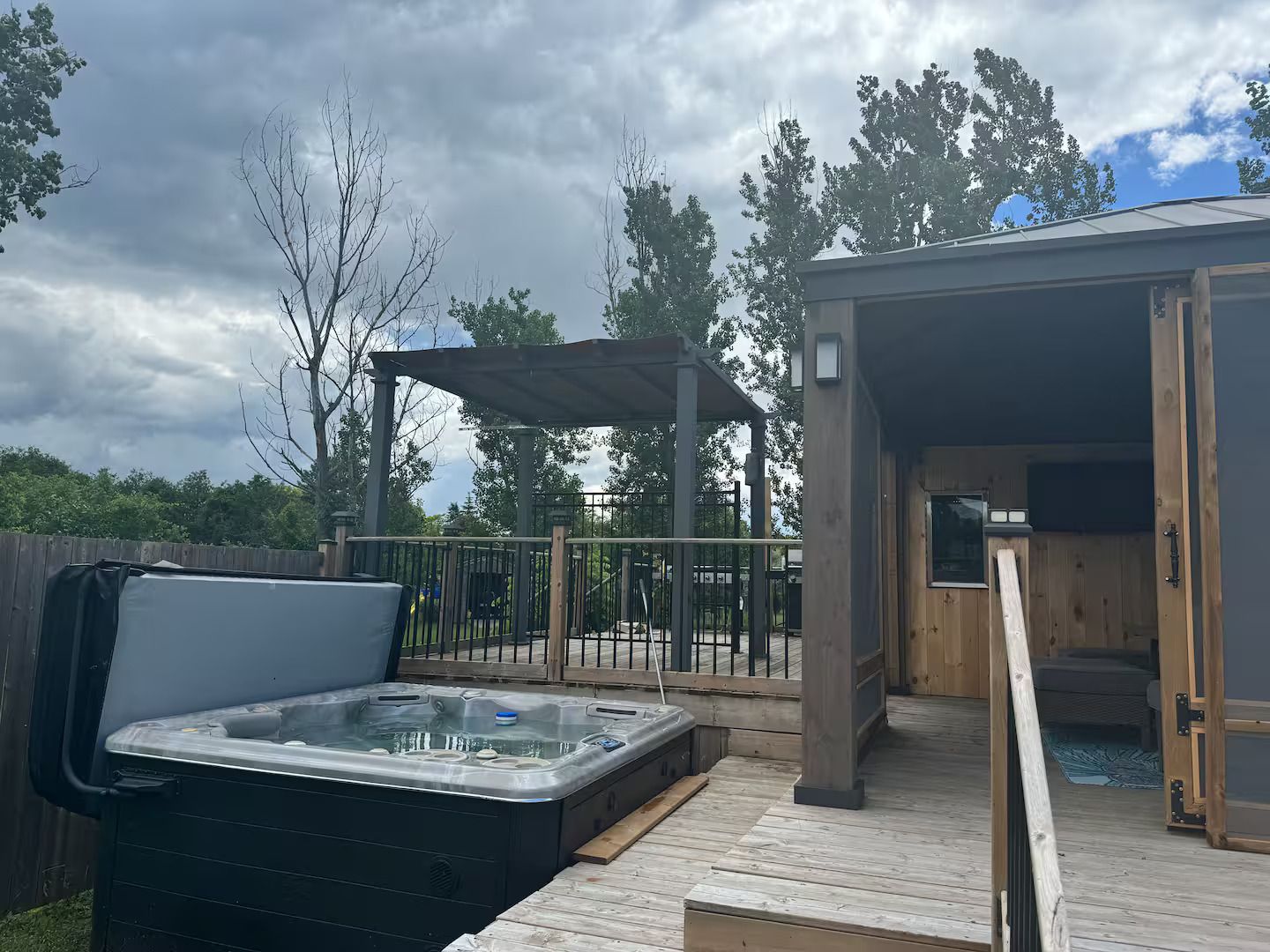 Un jacuzzi en una terraza de madera, un área de estar techada y un edificio con puerta abierta.