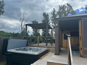 A hot tub on a wooden deck, a covered seating area, and a building with an open door.