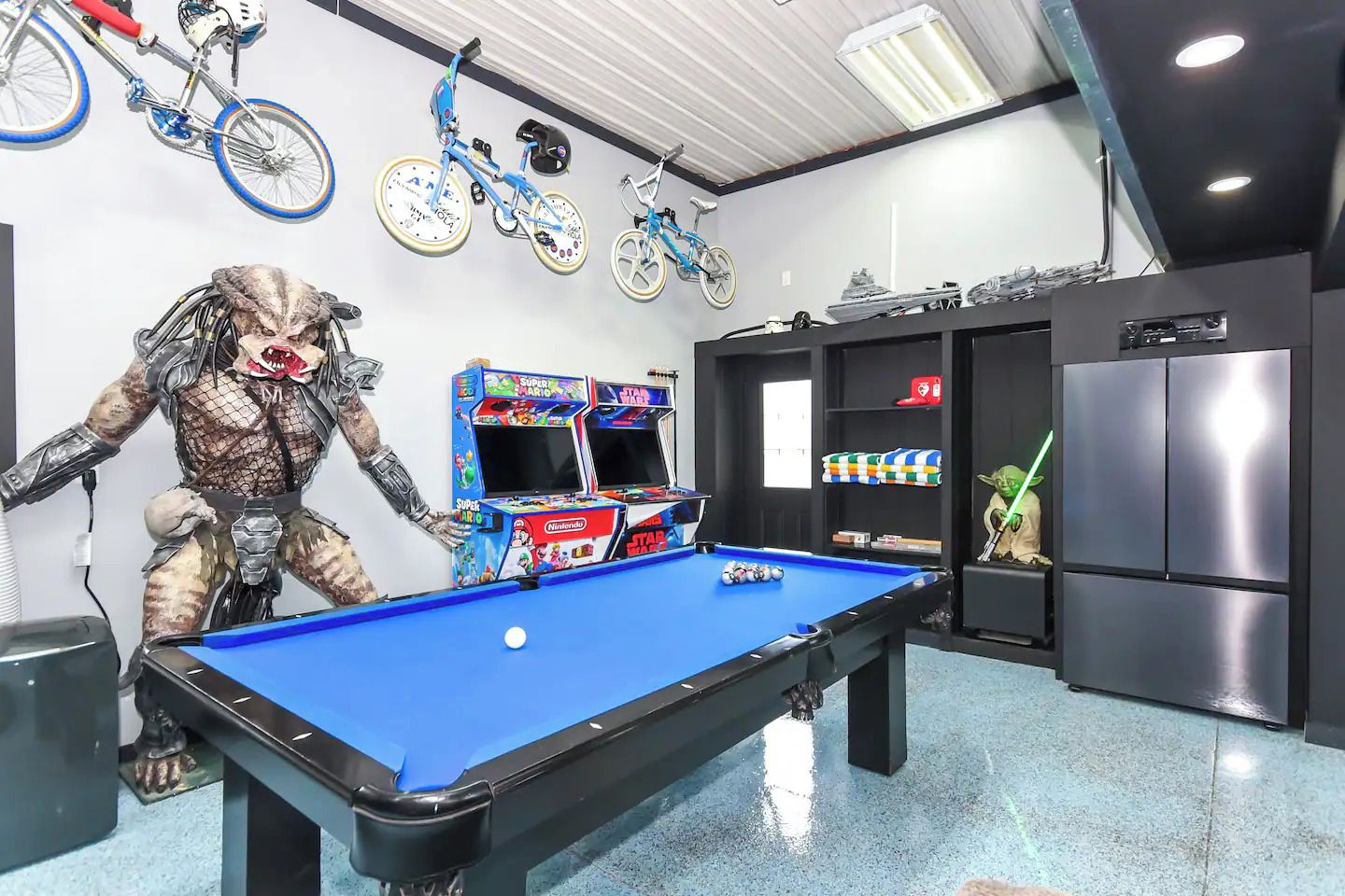 A pool table with a pool cue, a claw machine, and arcade games.