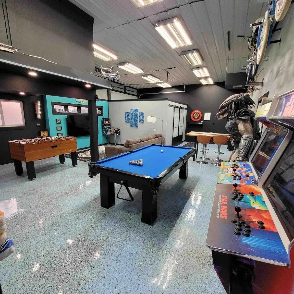 A recreational room with a pool table, foosball table, and a Star Wars-themed arcade machine.