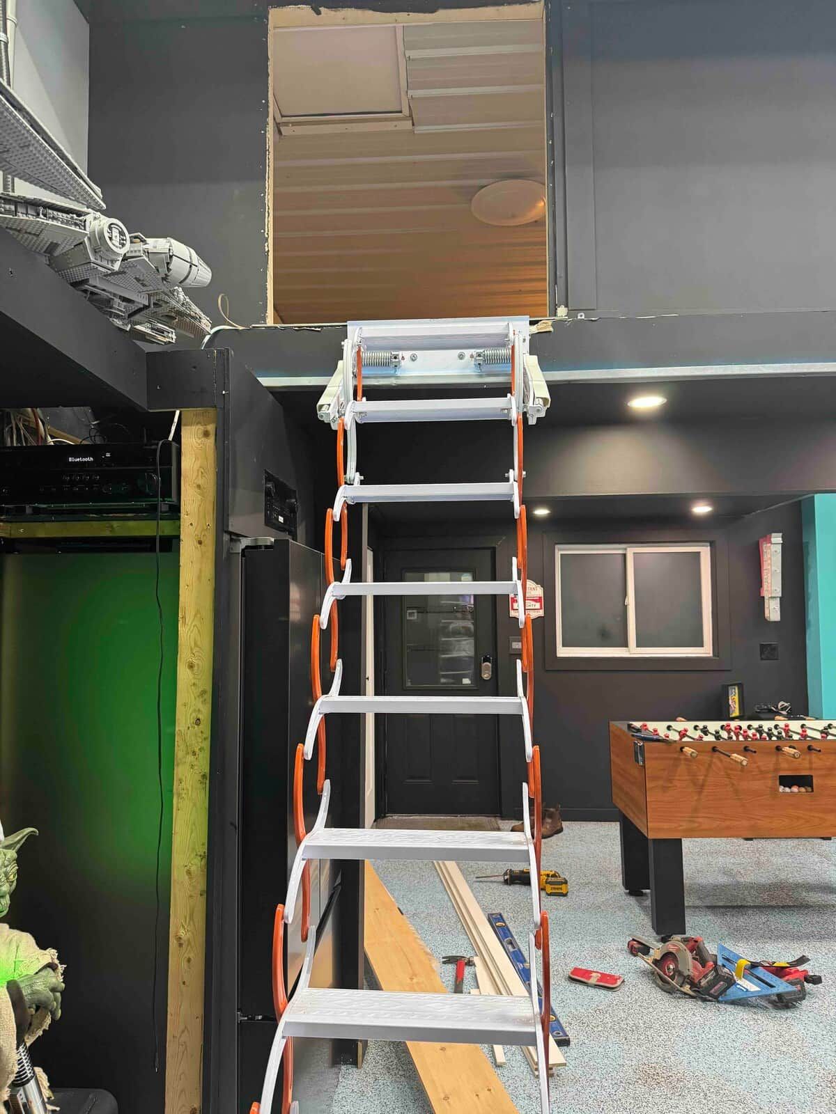 A room with a metal ladder, a foosball table, and construction materials on the floor.