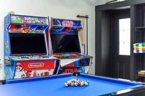 Two Nintendo arcade machines, one with Super Mario and the other with Star Wars, next to a pool table with billiard balls.