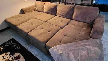 Ein Ecksofa in einem Wohnzimmer mit Couchtisch, Lampe und einem Essbereich im Hintergrund.