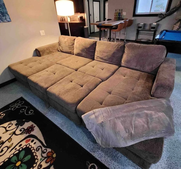 A sectional sofa in a living room with a coffee table, a lamp, and a dining area in the background.