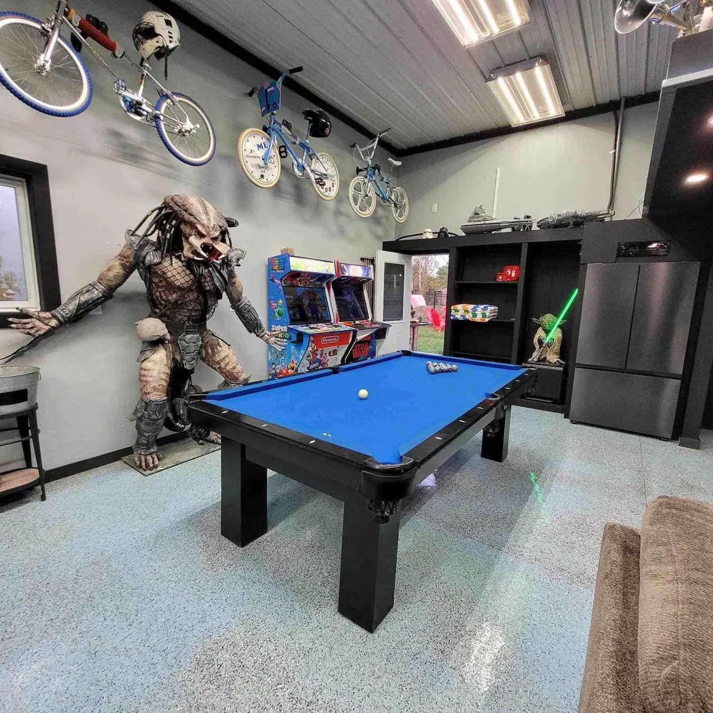 A pool table in a room with a large statue of a creature, bicycles, and a Star Wars figure.