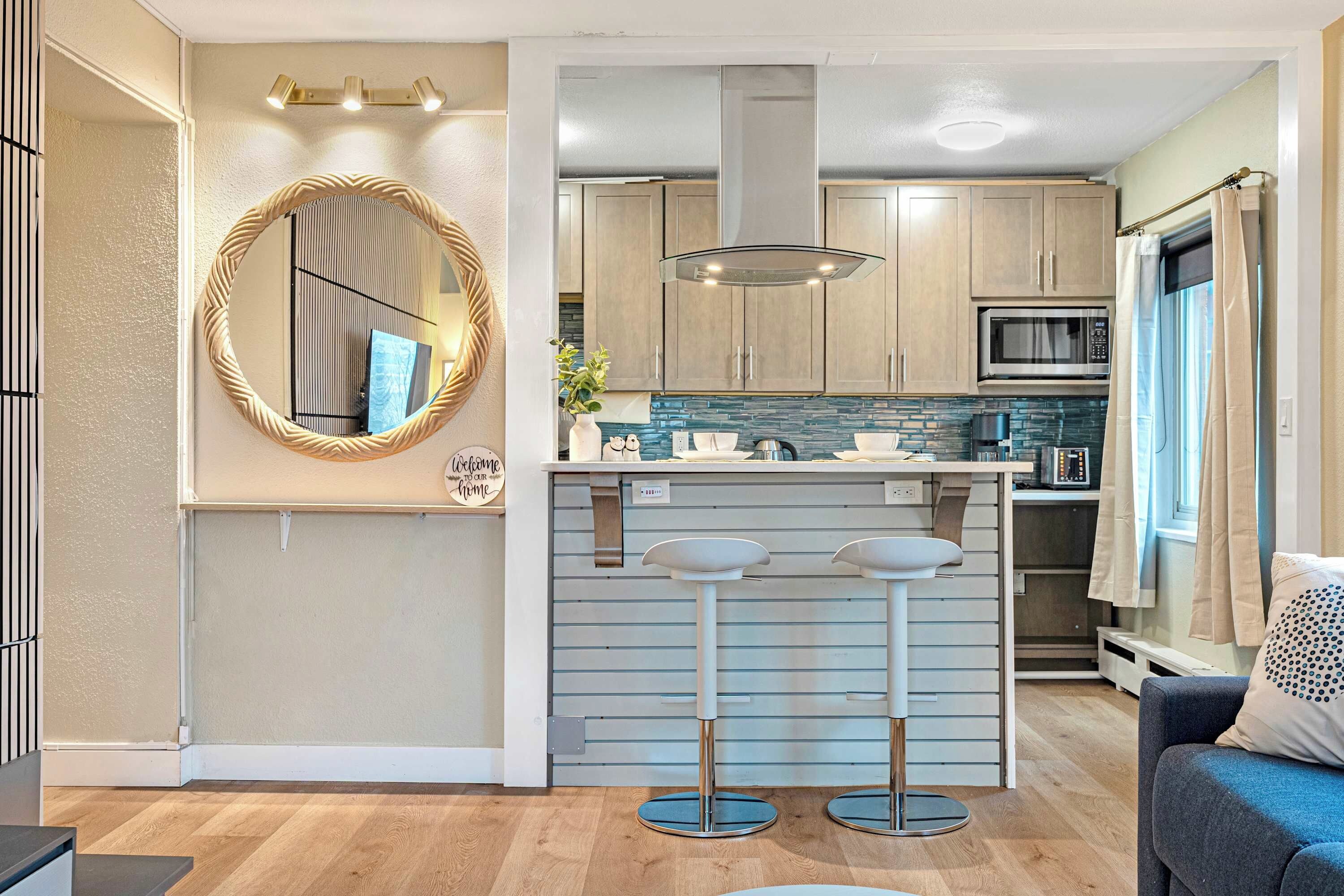 A compact kitchen with a microwave, stove, and bar stools.