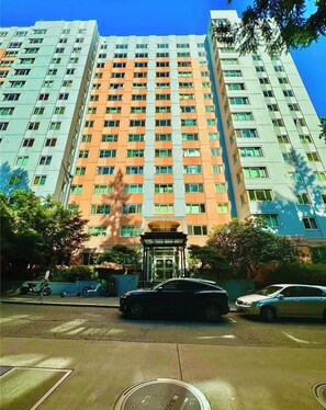 A multi-story building with a central entrance, surrounded by parked cars and trees. - Elektra (Seattle)