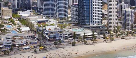 A coastal cityscape with high-rise buildings, a sandy beach, and a pool area.