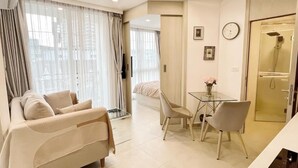 En moderne stue med sofa, spisebord med stole, en glasbrusekabine og en seng i baggrunden.