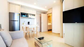 A modern kitchen with white cabinetry, a built-in microwave, and a coffee machine. There is a glass coffee table in the living area.