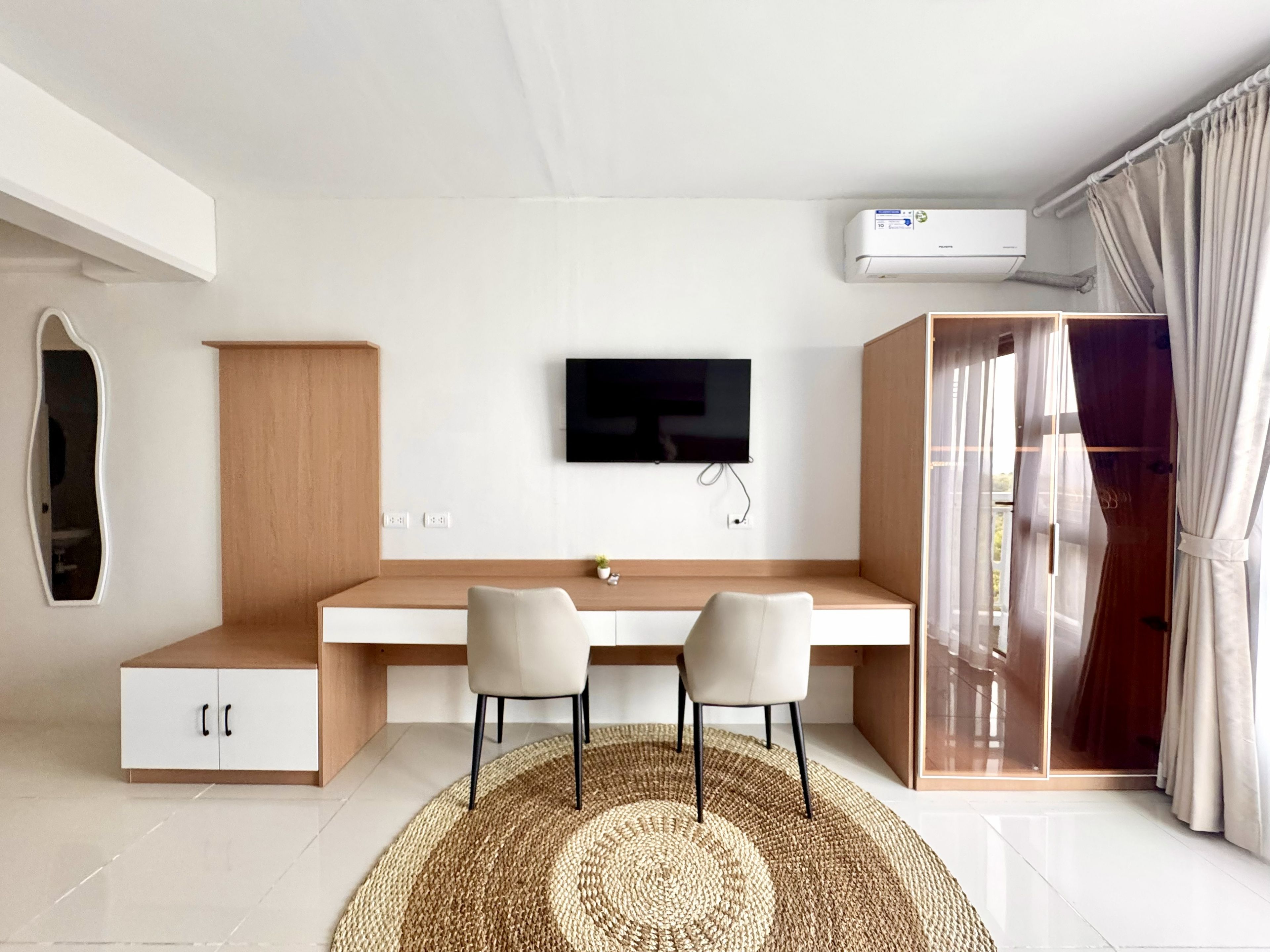 Une chambre moderne équipée d’un bureau, de deux chaises, d’une télévision et d’un appareil de climatisation.