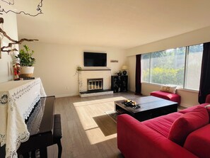 A living room with a fireplace, a television mounted above it, a red sofa, and a large window with curtains.
