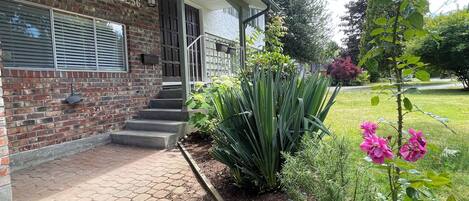 Una casa de ladrillo con el número '2256' en la pared, un porche cubierto y un jardín con diversas plantas y flores.