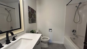 A bathroom with a white sink, toilet, and bathtub. There is a mirror above the sink and a showerhead above the bathtub. - Bright & Cozy - The White Rock Gateway (Surrey)
