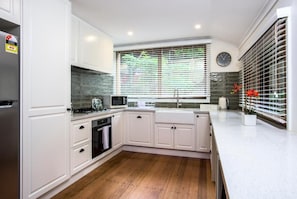 A modern kitchen with white cabinetry, a microwave, a stove, and a sink. - Camellia Cottage (Olinda)
