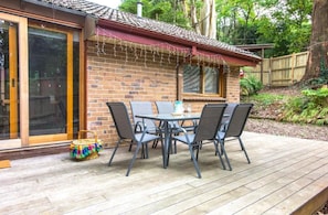 A patio with a table and chairs, a wicker basket, and a brick building with a red awning. - Camellia Cottage (Olinda)