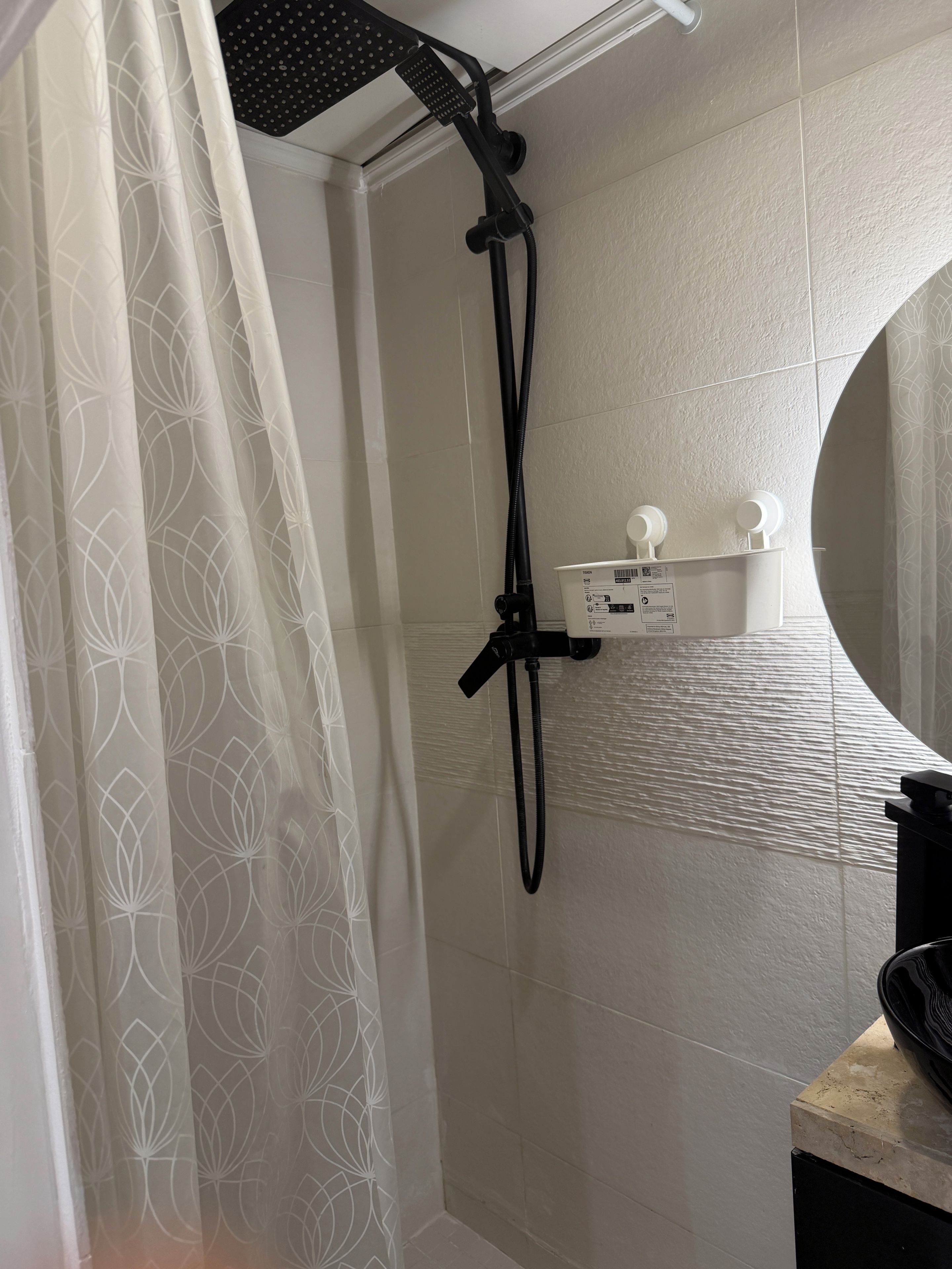 A shower area with a handheld showerhead, a wall-mounted control panel, and a toilet with a white lid.