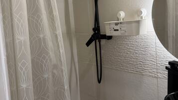 A shower area with a handheld showerhead, a wall-mounted control panel, and a toilet with a white lid.
