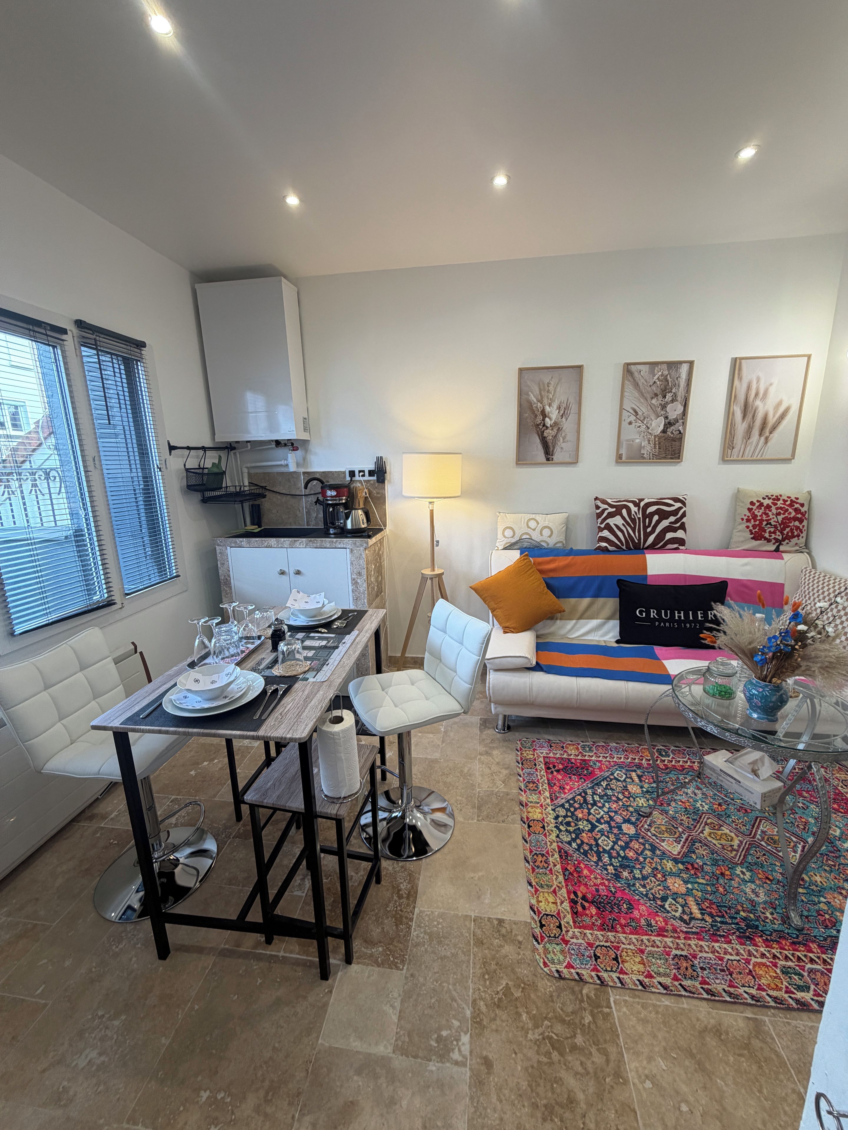 Een moderne woonkamer met een eetgedeelte, een bank met kleurrijke kussens en een kamerkleed met een patroon.