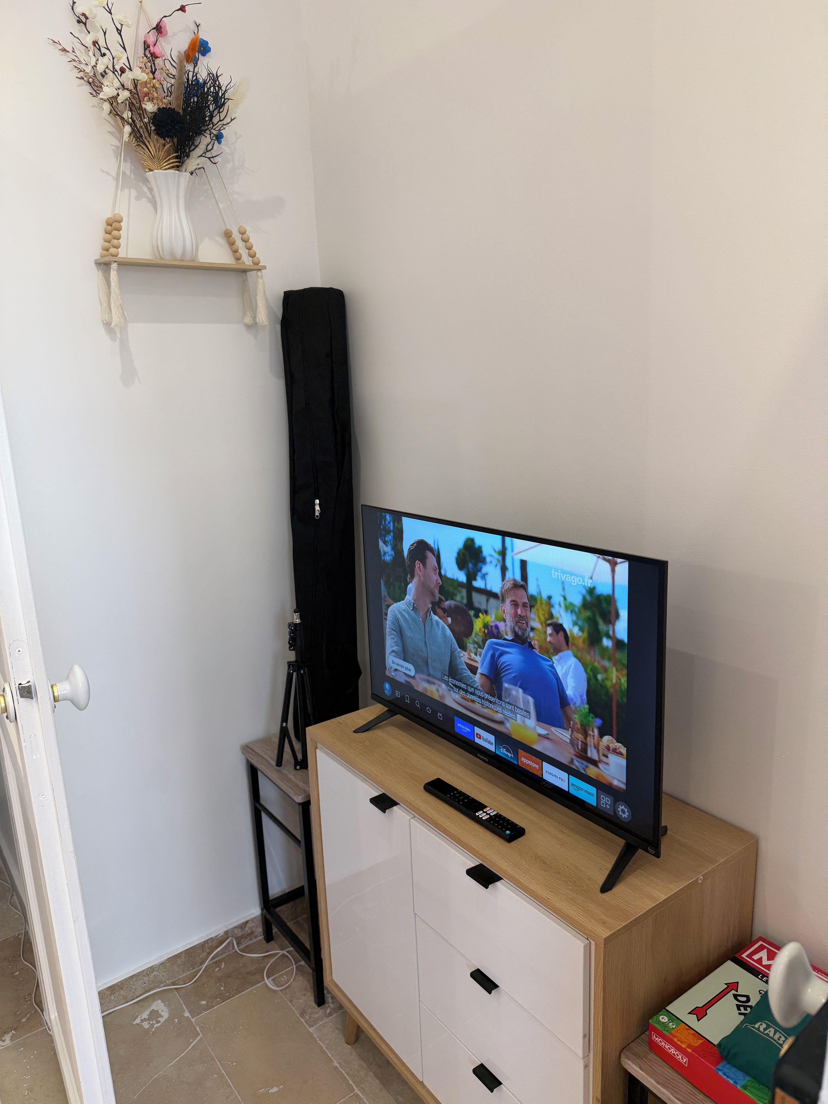 Un téléviseur posé sur un meuble en bois, un haut-parleur noir et une étagère ornée d’objets décoratifs.
