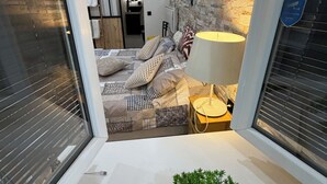 Une chambre à coucher moderne avec un mur en pierre, un lit avec une literie à motifs, une lampe de chevet et une petite plante en pot.