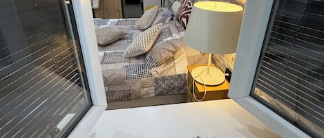 A modern bedroom with a stone wall, a bed with patterned bedding, a bedside lamp, and a small potted plant.