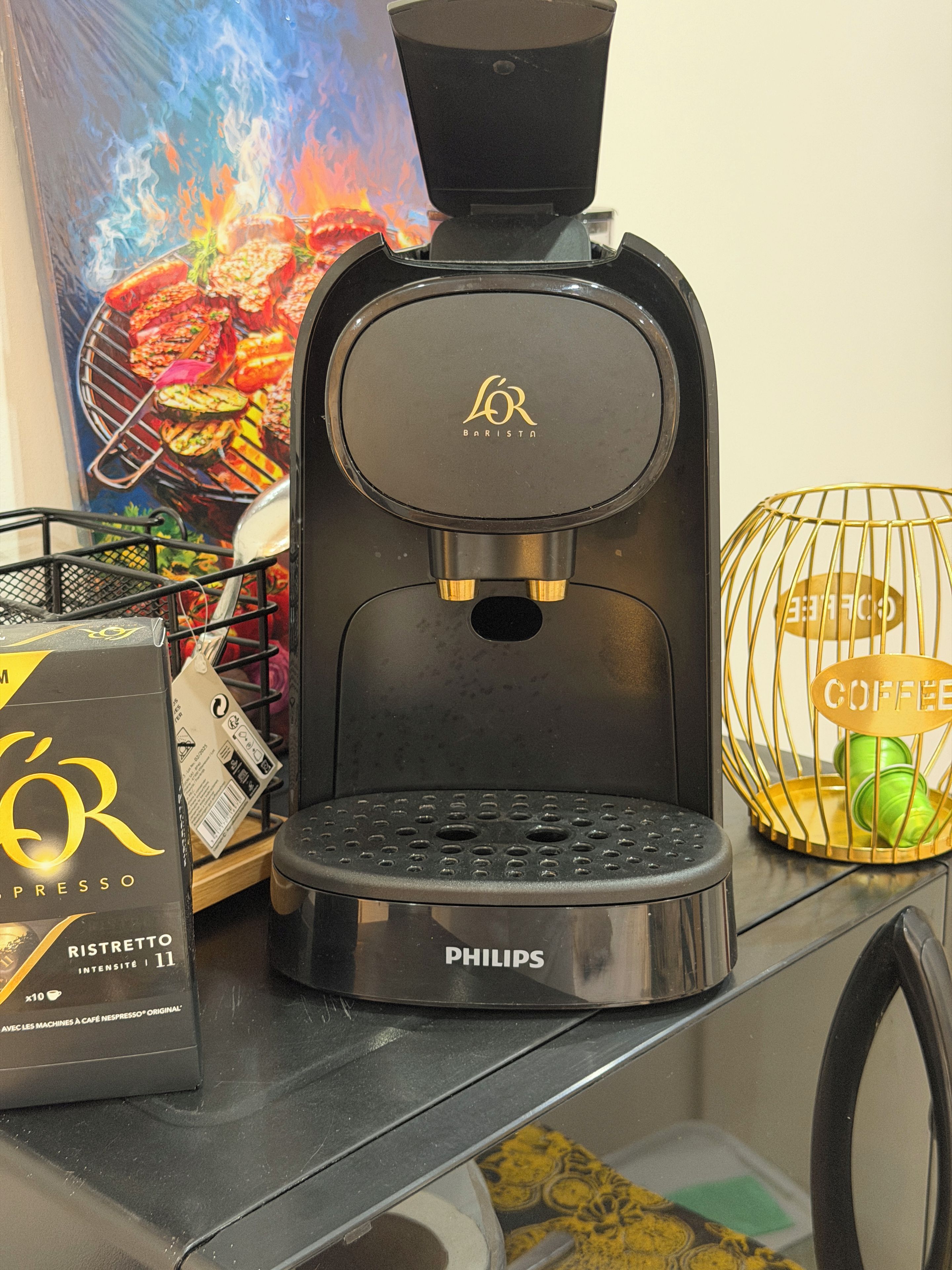 Eine Kaffeemaschine mit Firmenlogo, einer Tassehalterung und einer Kaffeeverpackung auf einer Arbeitsfläche.