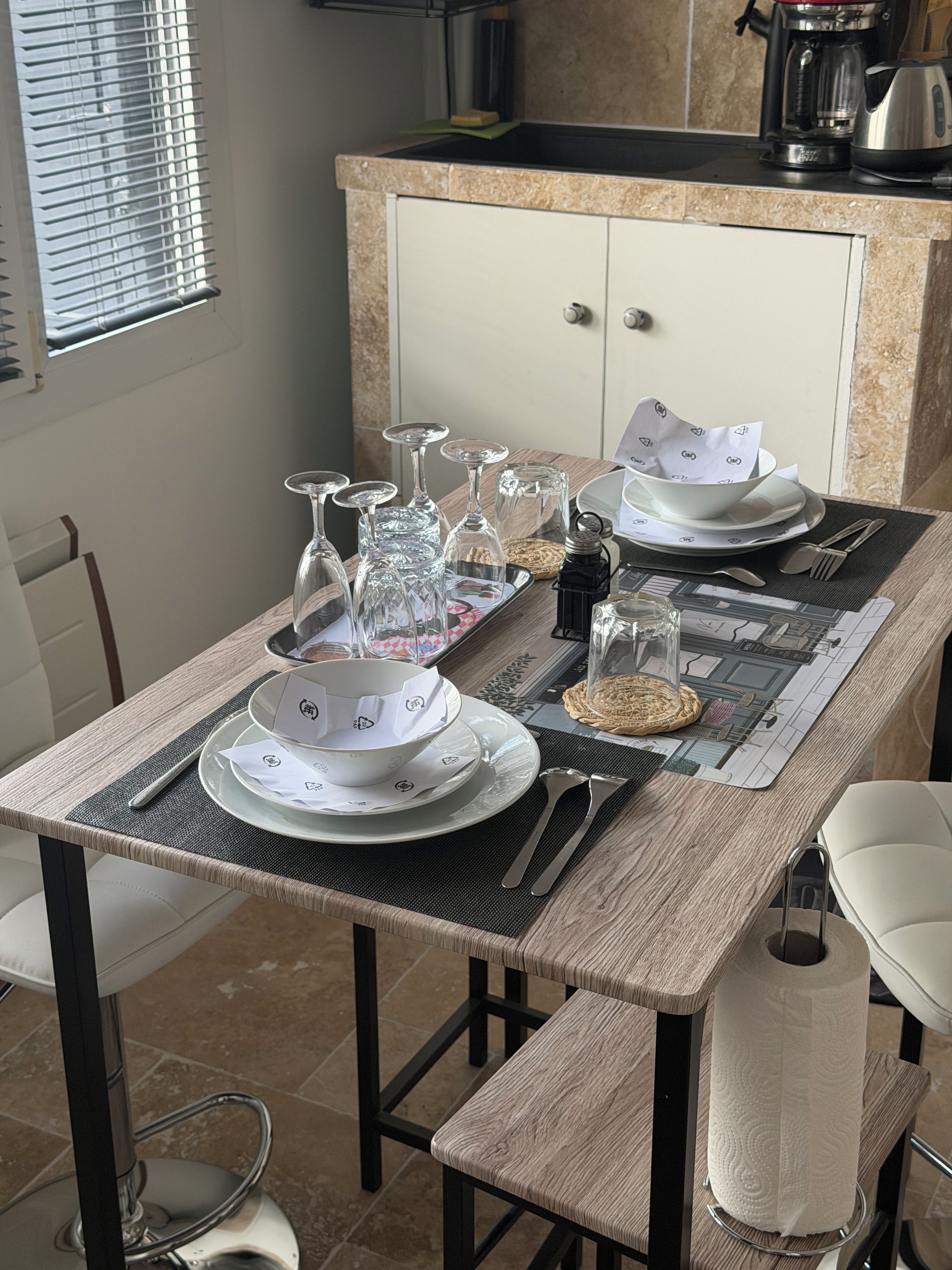 Een eettafel gedekt met borden, glazen, bestek en een servetdispenser.