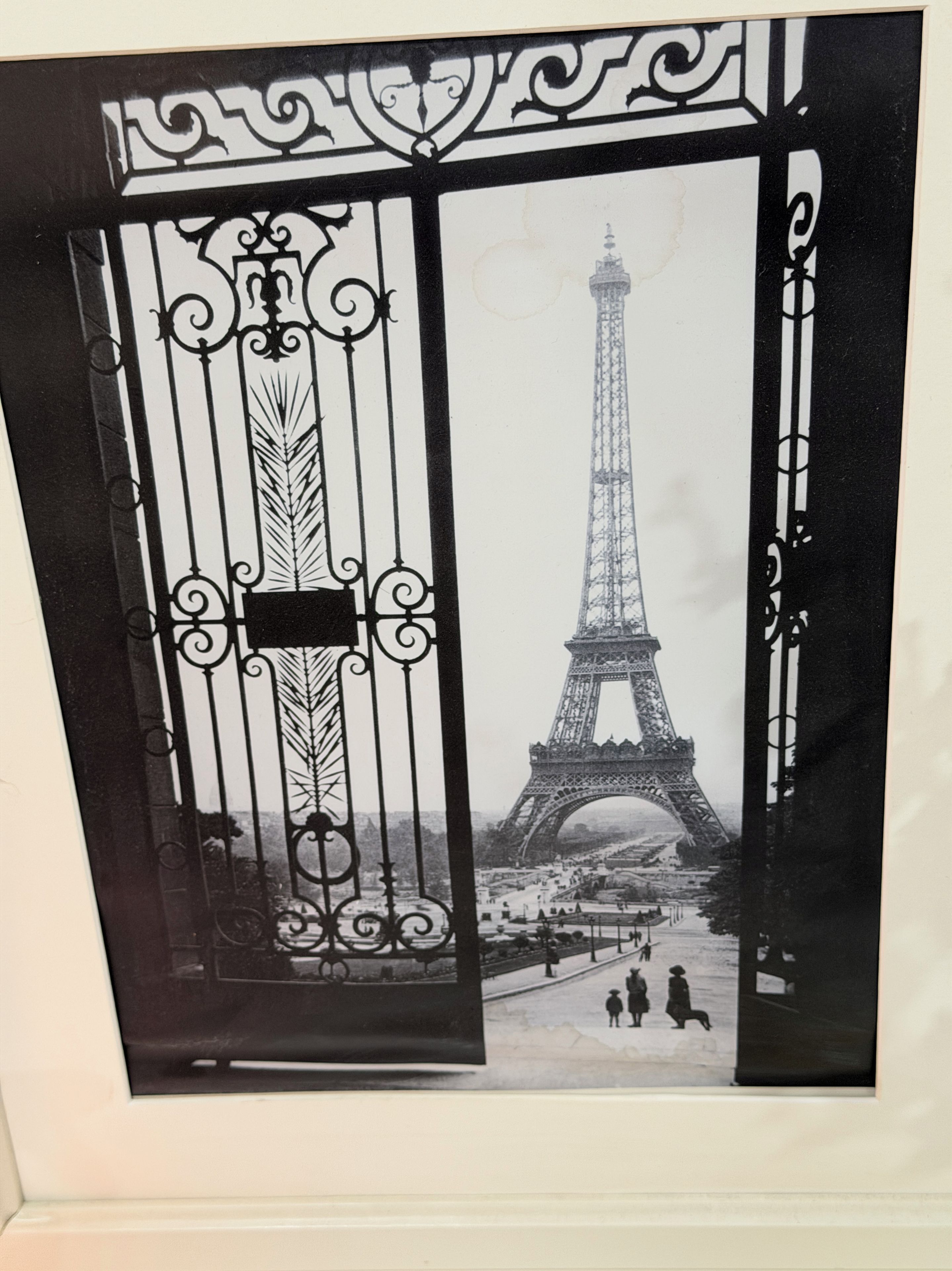 Een zwart-witfoto van de Eiffeltoren, te zien door een sierijzeren hek.