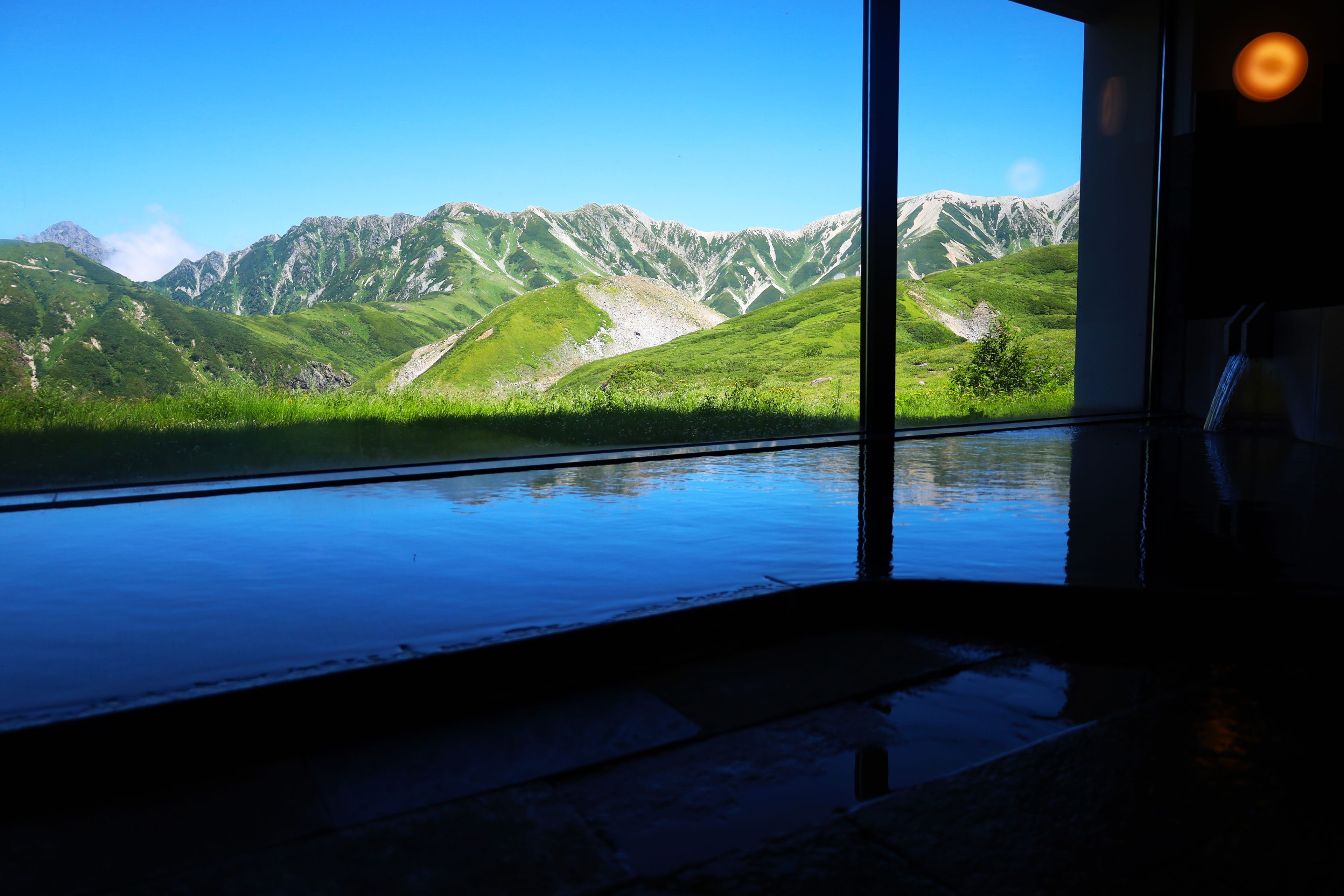 A room with a large window offering a view of green mountains and a clear sky.