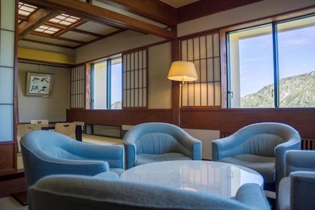 A traditional Japanese-style room with tatami flooring, low wooden beams, and shoji screens. There are two blue armchairs and a small round table.