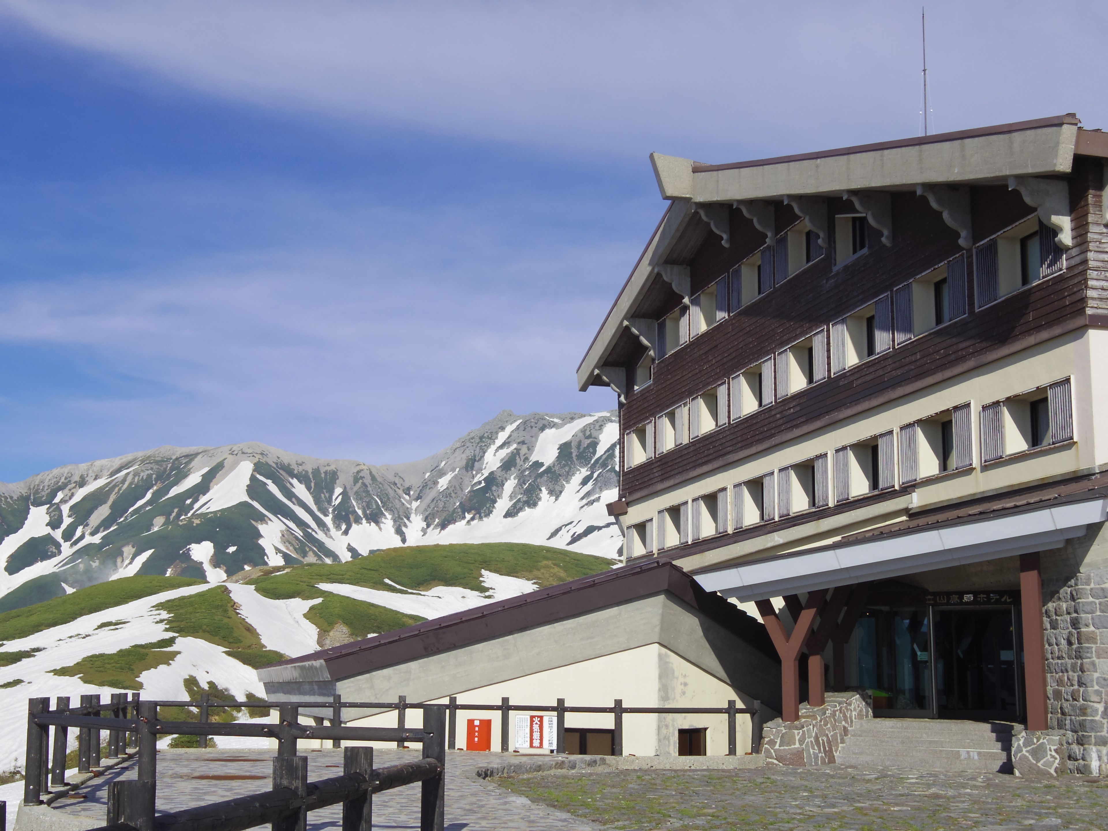 Un hotel con el paisaje de montañas de fondo, que presenta un estilo arquitectónico tradicional con una entrada destacada y fachada de piedra.