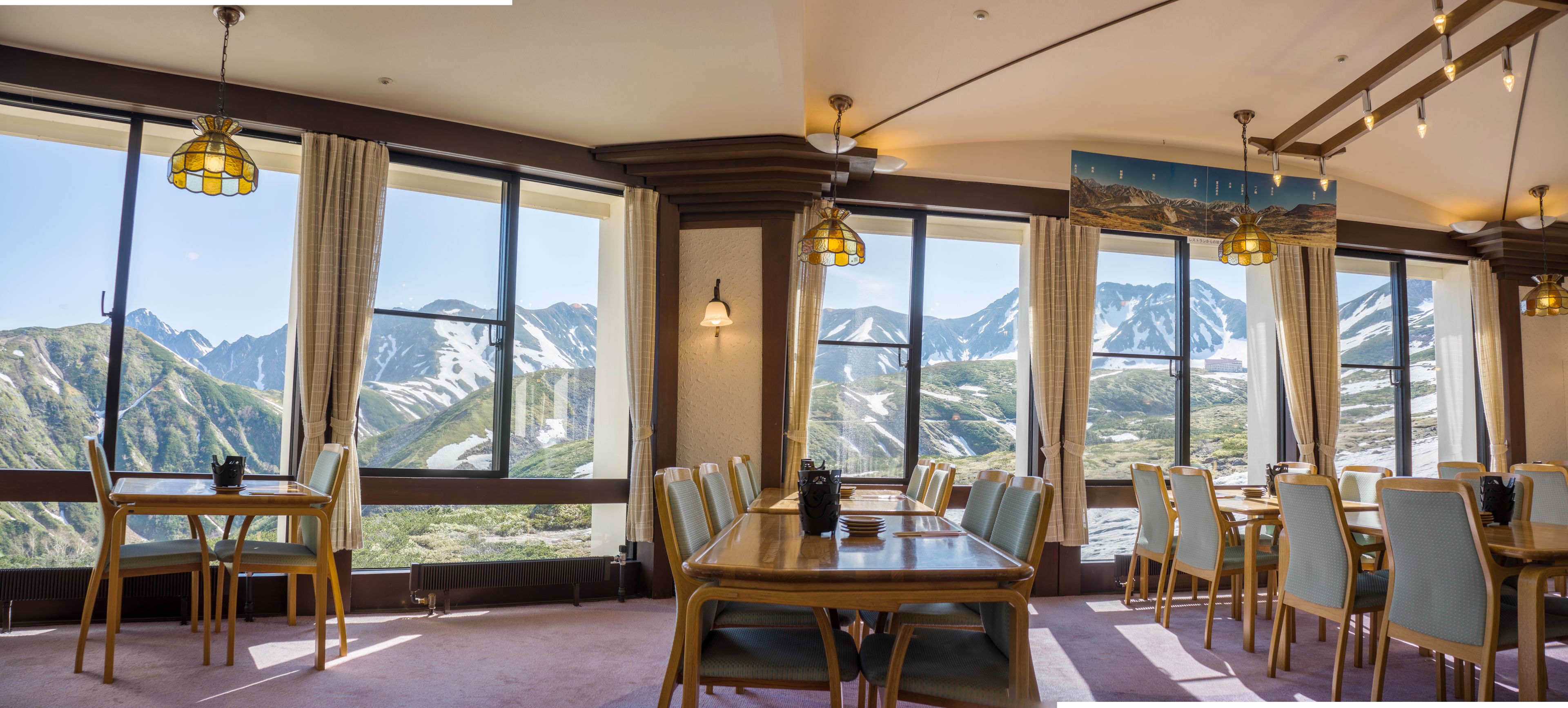 Un comedor con vistas a la montaña, ventanas amplias y mobiliario de madera.