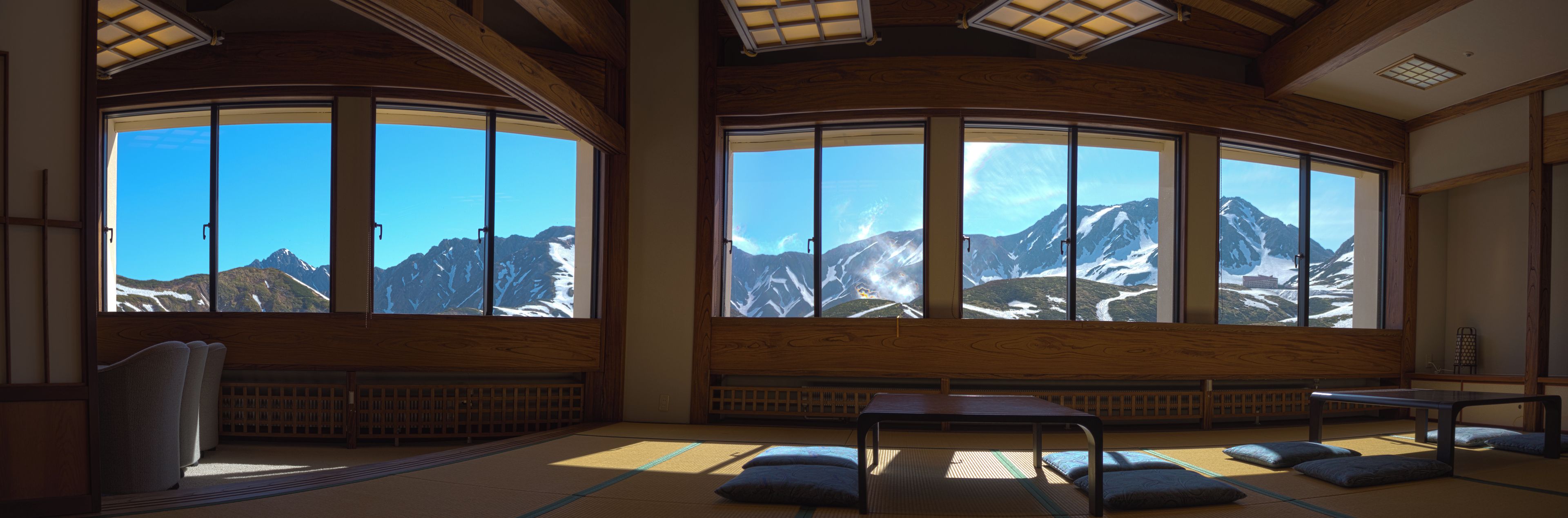 A traditional room with tatami flooring, a low table, and large windows offering mountain views.
