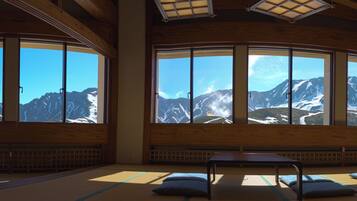 A traditional room with tatami flooring, a low table, and large windows offering mountain views.