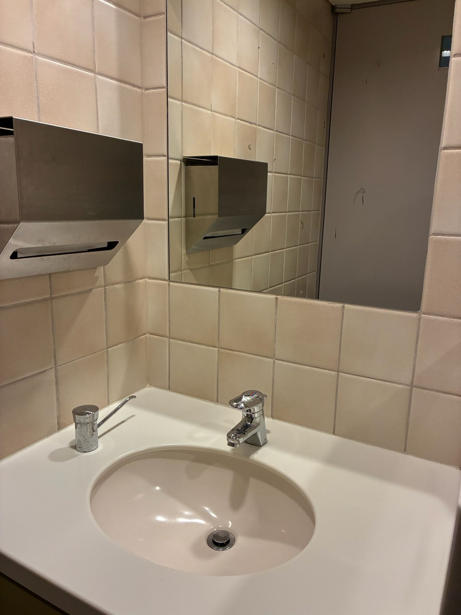 A bathroom with a sink, mirror, and towel dispenser.