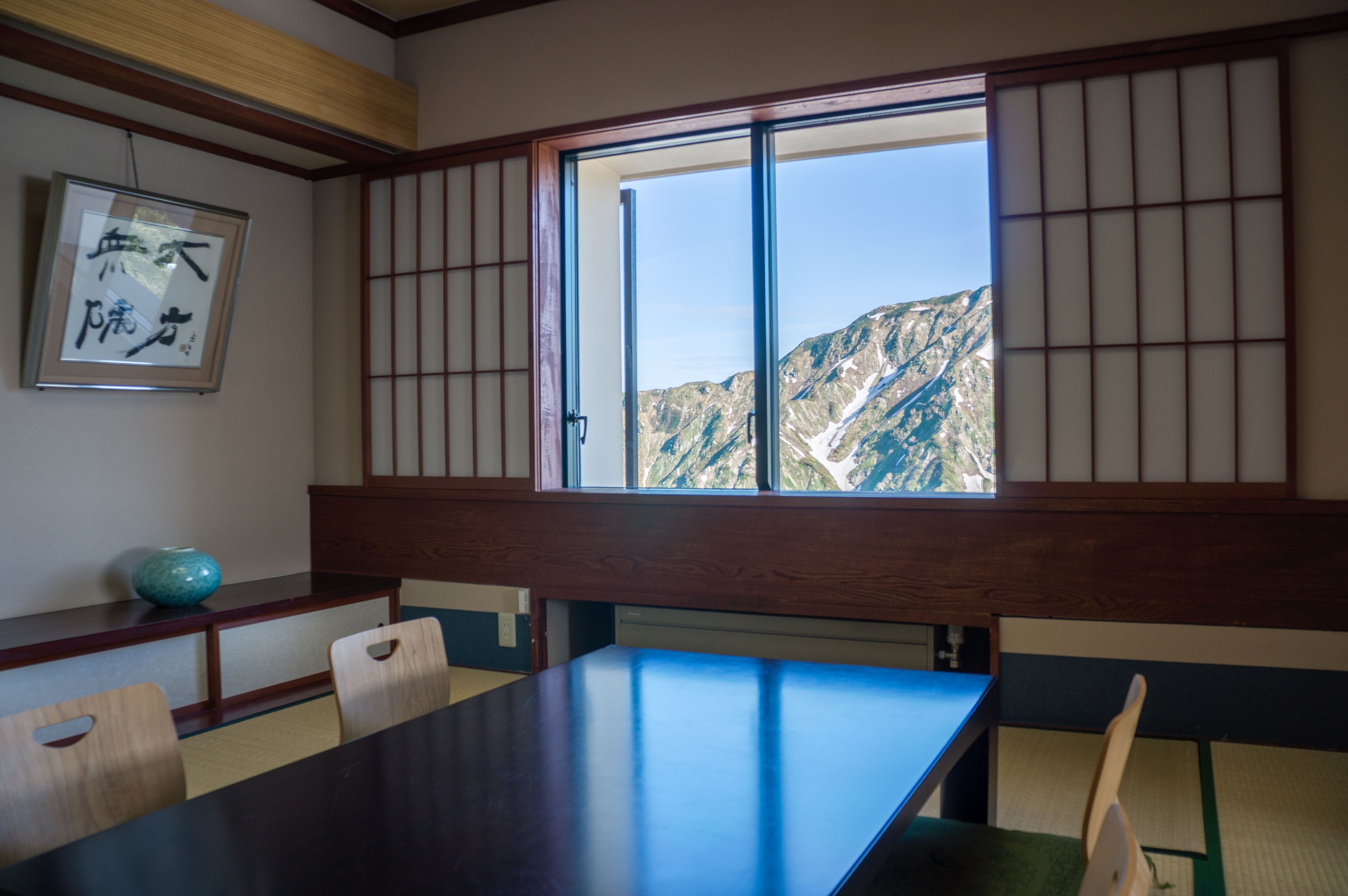 A traditional Japanese room with tatami flooring, a low wooden table, and a large window offering a mountain view.
