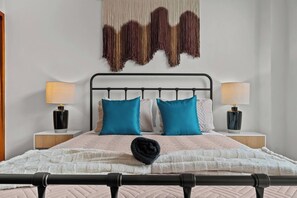 A neatly made bed with a headboard, two bedside lamps, and a wall hanging. - Grand Galleria — Old San Juan Private Patio (San Juan)