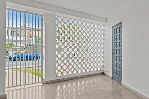 Ein Zimmer mit einer weißen Tür, einer weißen Wand mit geometrischem Muster und Blick auf eine Straße mit einem blauen Auto.
