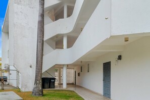 A white building with a curved balcony, a door, and a trash bin. - Private Patio 2BR Near Ocean Park Beach (San Juan)