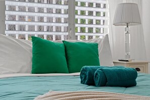 A bed with green and white pillows, a teal bedspread, and a rolled-up teal towel. - Private Patio 2BR Near Ocean Park Beach (San Juan)