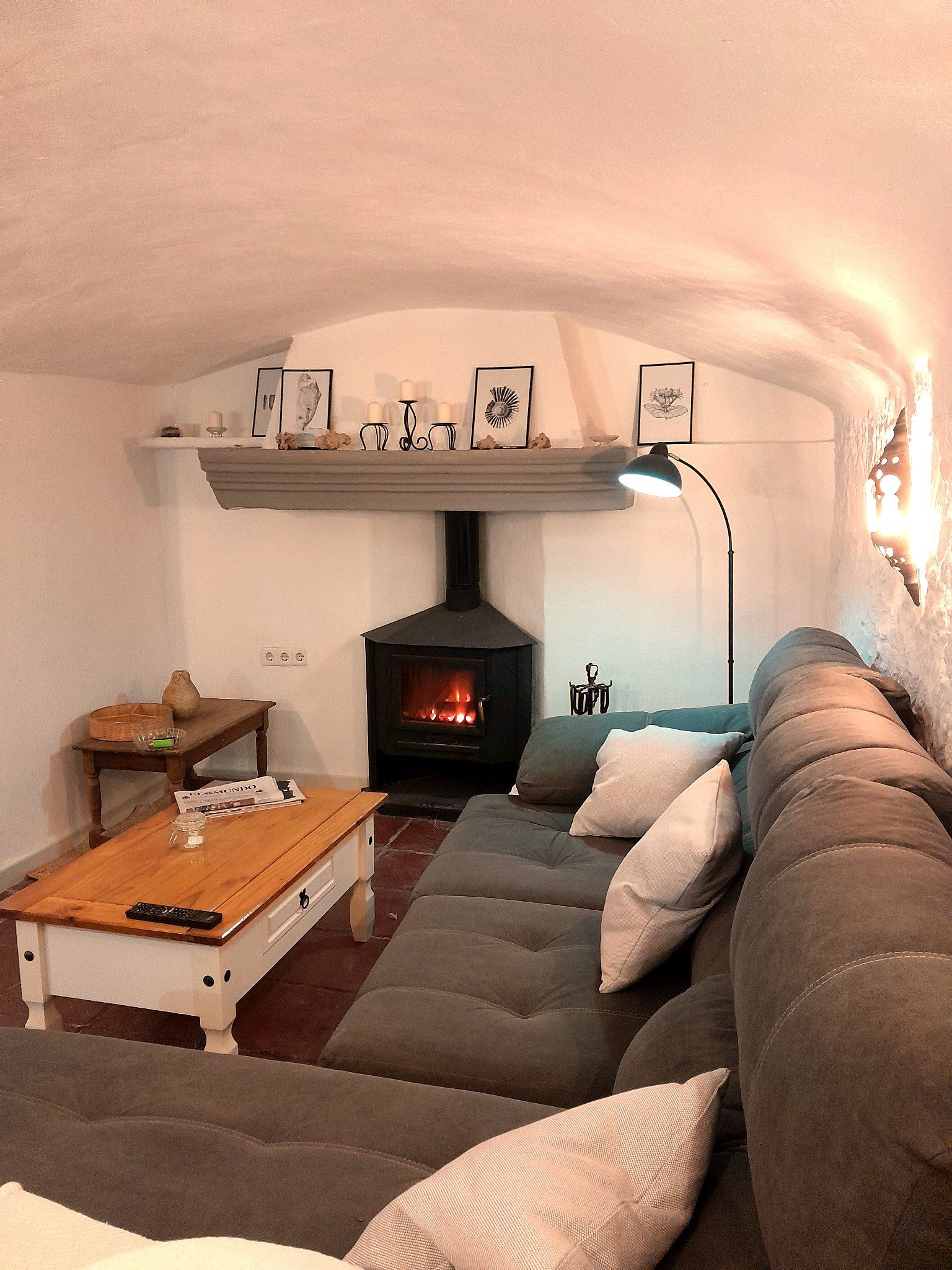 Een gezellige woonkamer met een stenen openhaard, een bank, een bijzettafeltje en lijstwerken aan de muur.