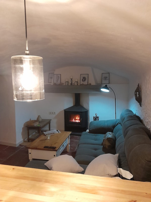 A cozy living room with a fireplace, a sofa, a coffee table, and a hanging light fixture.