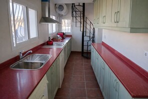 A kitchen with a red countertop, stainless steel sink, and a spiral staircase.
