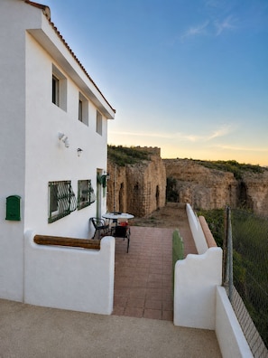 A white building with a patio area, outdoor furniture, and a view of a rocky landscape.