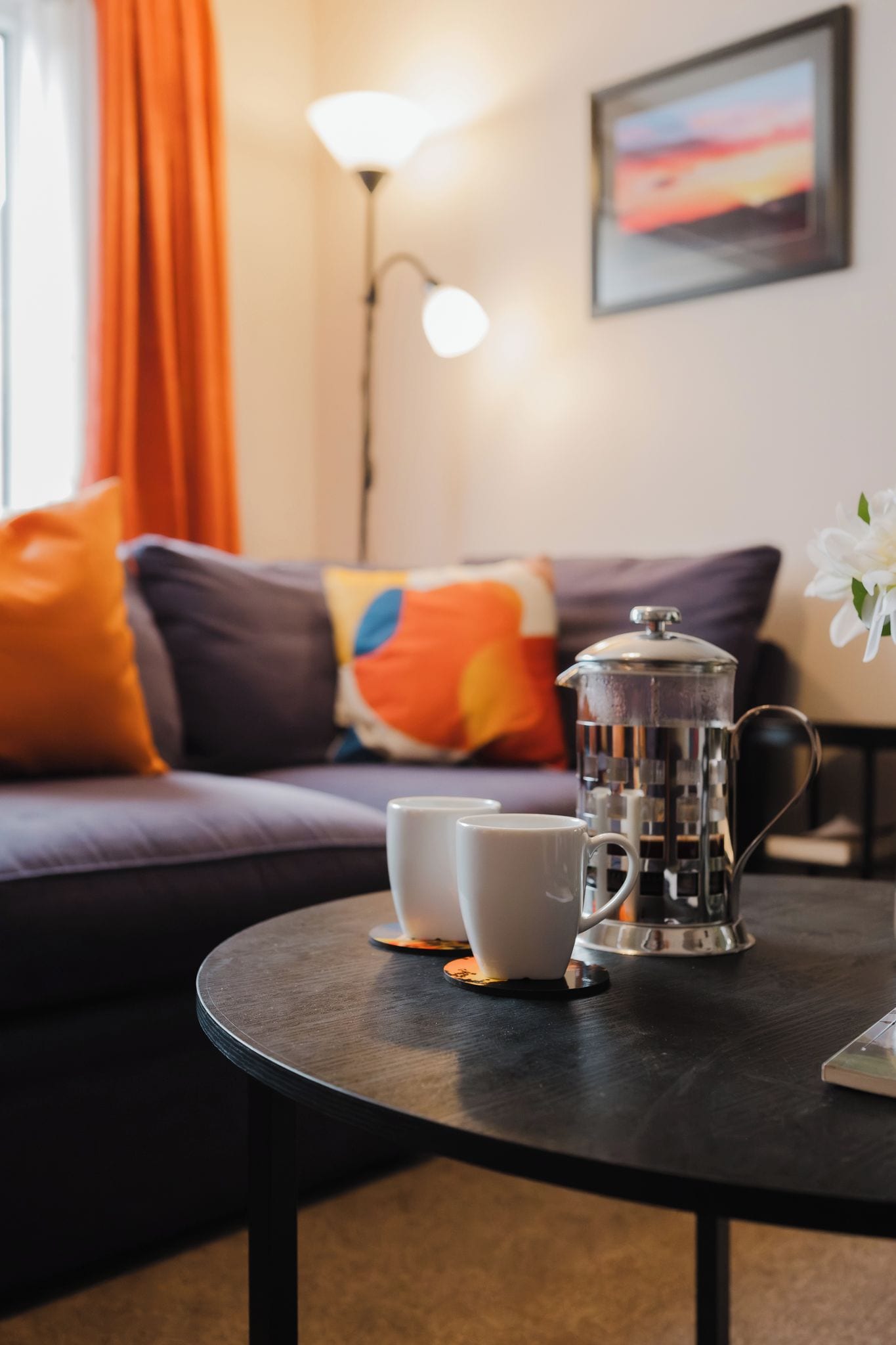 Ein runder Tisch mit einer Kaffeemaschine, zwei weißen Tassen und einer Blume.