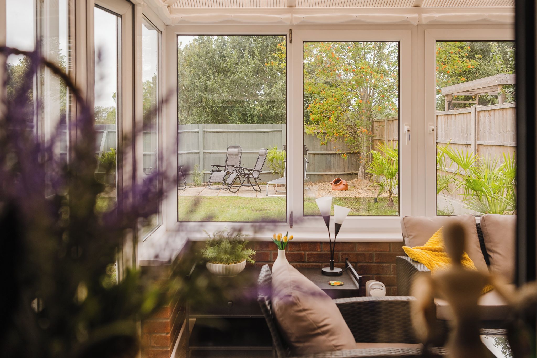 Un invernadero con vistas a un jardín trasero, que incluye un patio con asientos y una mesa.