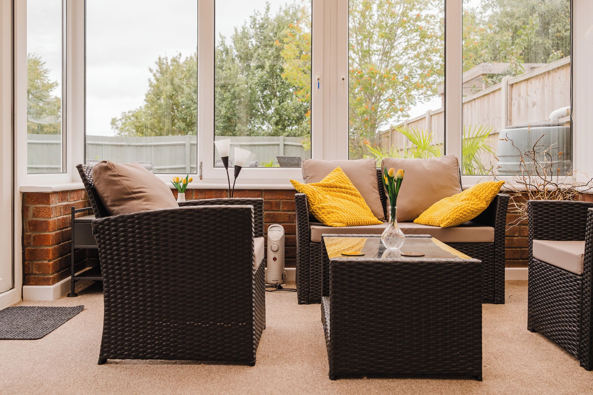 A sunlit outdoor seating area with wicker furniture, a brick wall, and a view of a garden.