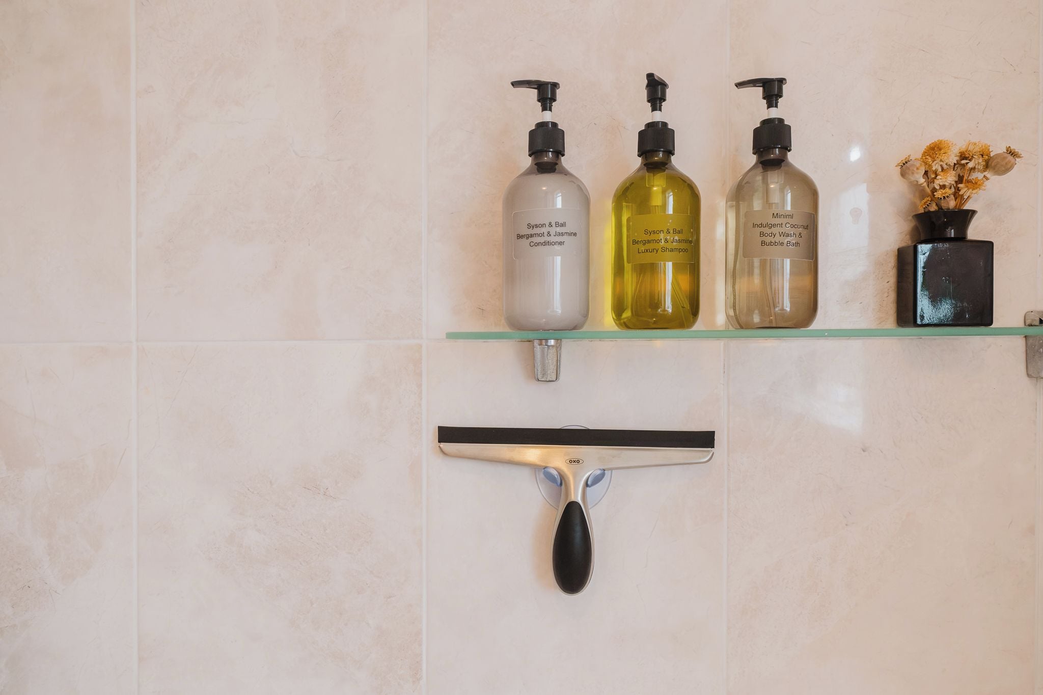 Een badkamerplank met drie flesjes shampoo en conditioner, een douchegel en een rakel.