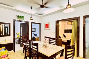 A dining area with a table, chairs, ceiling fan, pendant lights, and a view into a bedroom. - Nivera Stays 4BHK Ground Floor Home near Fortis, IGI Airport, South Delhi (New Delhi)